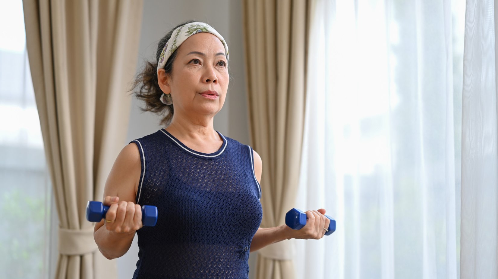 Active middle aged woman exercising with dumbbells in bright